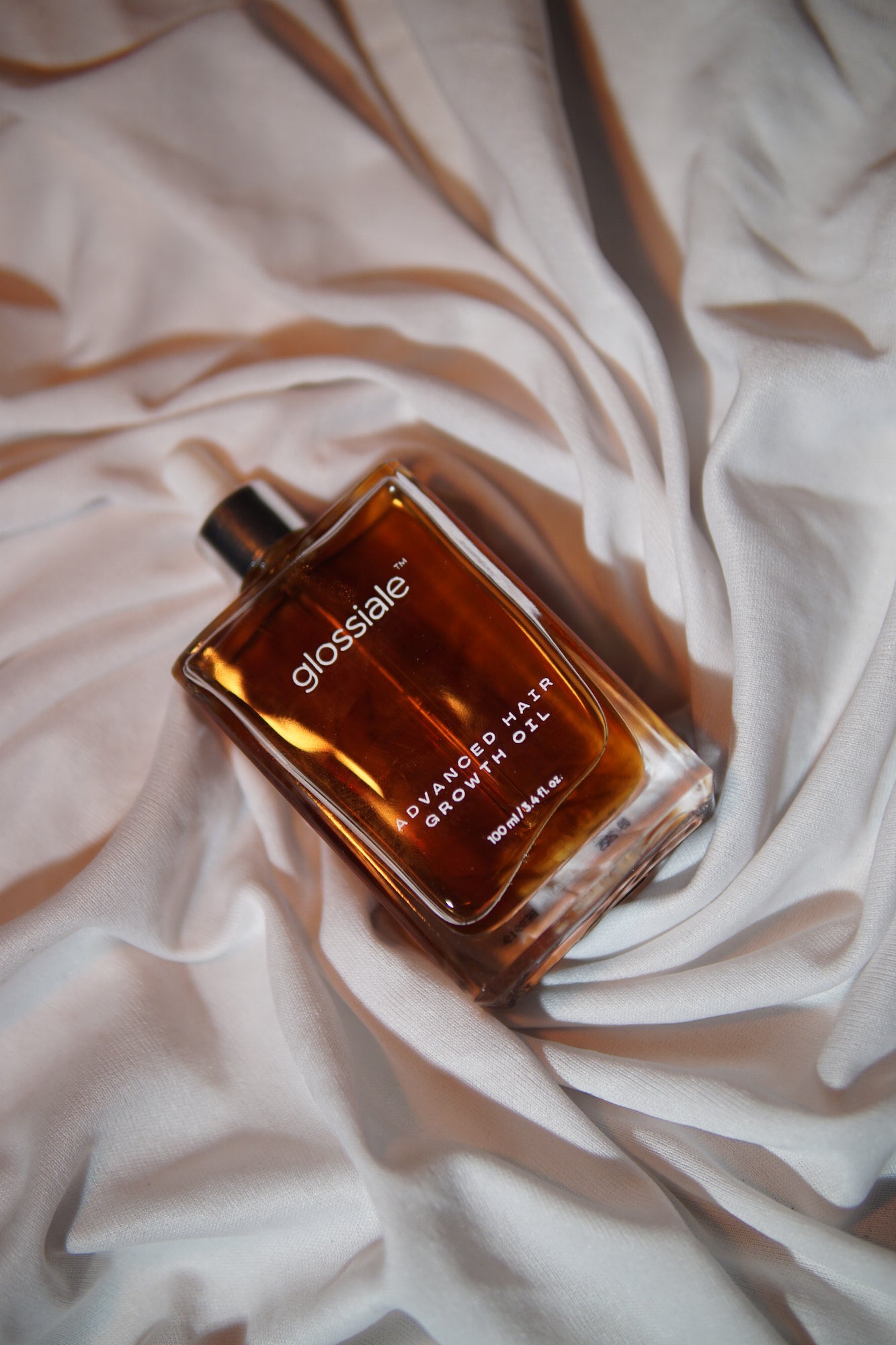 Glossiale Advanced Hair Growth Oil bottle on a white fabric background